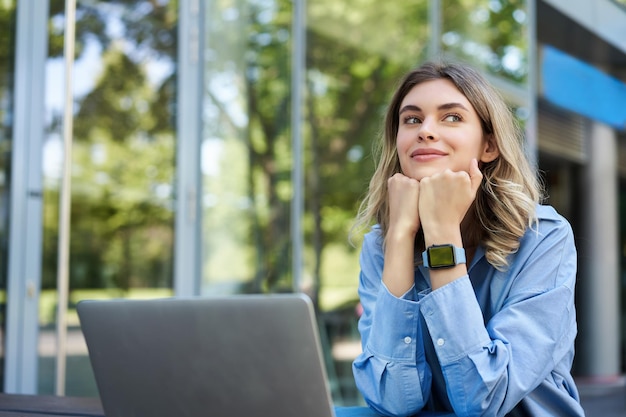 Retrato de una joven empresaria que trabaja al aire libre freelancer sonriendo sentada con una laptop fuera de bu