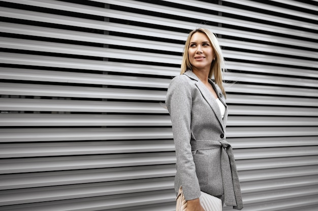 Retrato de joven empresaria rubia en traje gris caminando en la ciudad