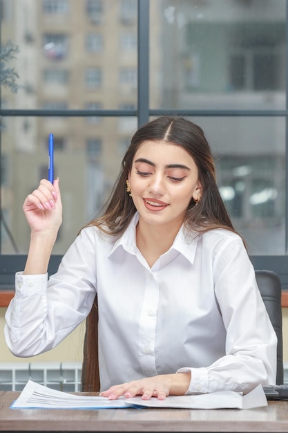 Retrato de una joven empresaria sentada en el escritorio y levantando su pluma