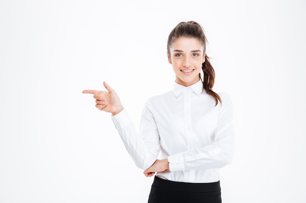 Retrato de una joven empresaria sonriente apuntando con el dedo hacia la pared blanca y mirando al frente