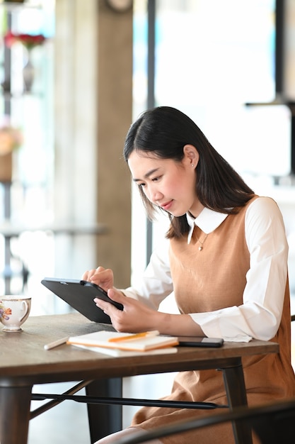 Retrato de joven empresaria con tableta digital mientras está sentado en la cafetería moderna.