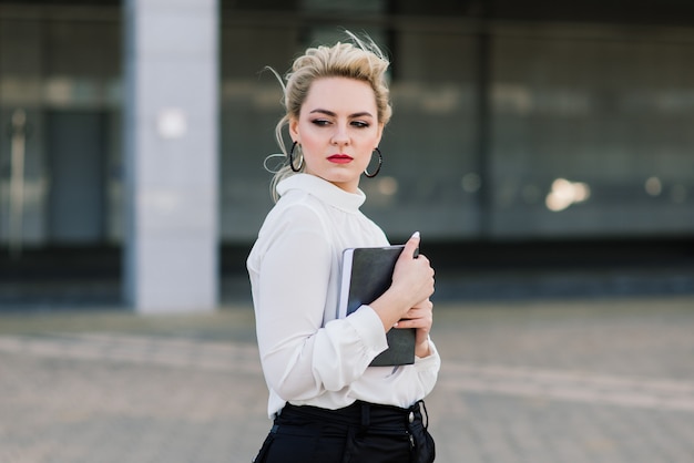 Retrato de una joven empresaria con teléfono, portátil, tableta, café al aire libre. Chica rubia en guantes de goma azul.