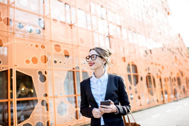 Retrato de una joven empresaria en el traje de pie al aire libre en el fondo de la pared de la oficina moderna