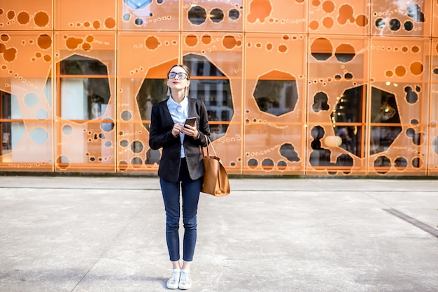 Retrato de una joven empresaria en el traje de pie al aire libre en el fondo de la pared de la oficina moderna