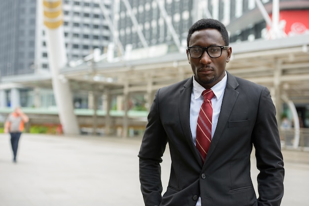 Retrato de joven empresario africano guapo en traje contra la vista del edificio moderno en la ciudad al aire libre