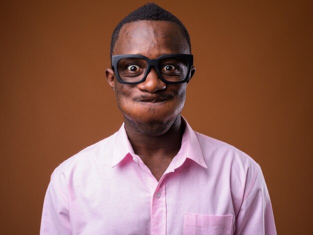 Retrato de joven empresario africano haciendo muecas contra la pared marrón