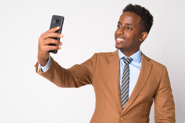 Retrato de joven empresario africano con pelo afro en traje marrón contra la pared blanca
