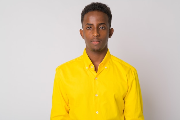 Retrato de joven empresario africano con pelo afro vistiendo camiseta amarilla contra la pared blanca