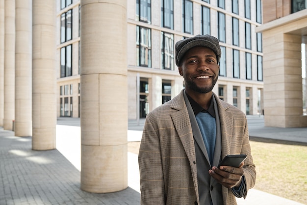 Retrato de joven empresario africano sonriendo a la cámara mientras está de pie en la ciudad