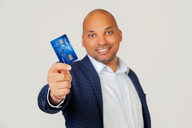 Retrato de un joven empresario afroamericano feliz sosteniendo una tarjeta de crédito con una cara feliz, se encuentra y sonríe con una sonrisa segura mostrando los dientes.