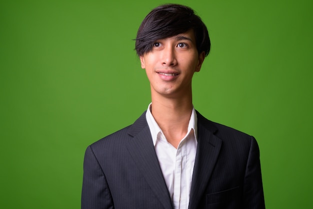 Retrato de joven empresario asiático contra la pared verde