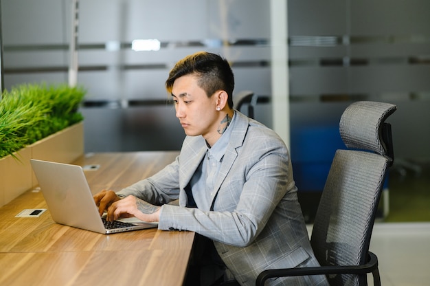 Retrato de un joven empresario asiático es inteligente y guapo con traje sentado en una silla mientras se siente confiado con una sonrisa como una sonrisa en la cara mirando a la cámara con una computadora portátil con fotos de alta calidad