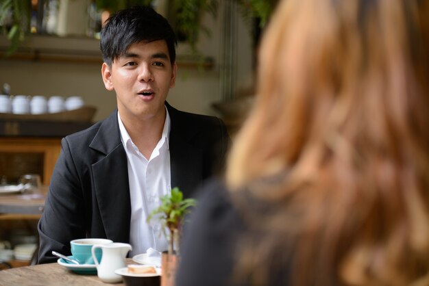 Retrato de joven empresario asiático y joven empresaria asiática juntos relajándose en la cafetería.