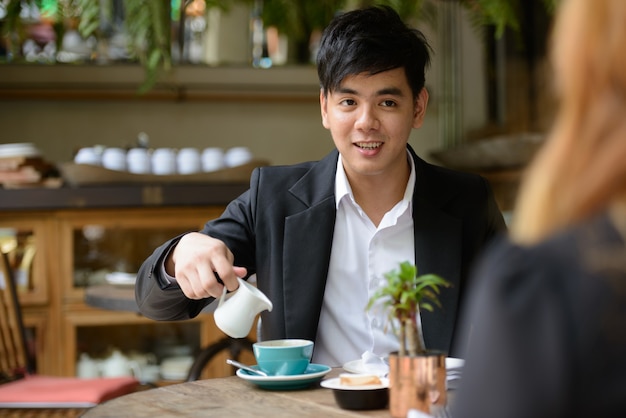 Retrato de joven empresario asiático y joven empresaria asiática juntos relajándose en la cafetería.