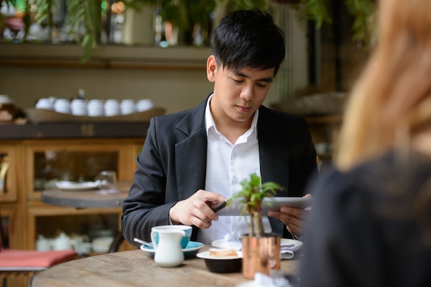 Retrato de joven empresario asiático y joven empresaria asiática juntos relajándose en la cafetería.