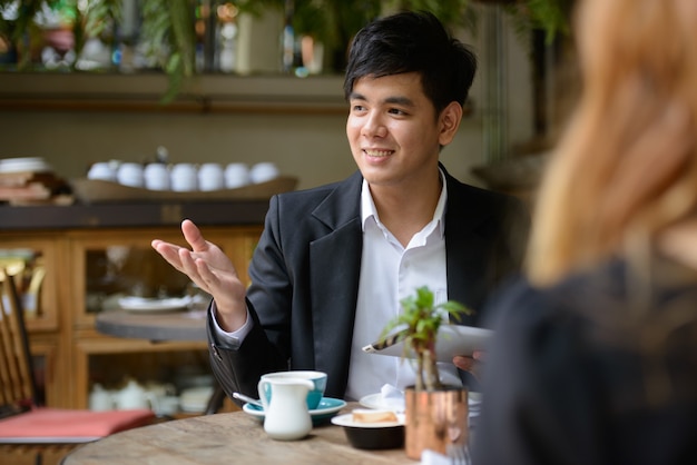 Retrato de joven empresario asiático y joven empresaria asiática juntos relajándose en la cafetería.