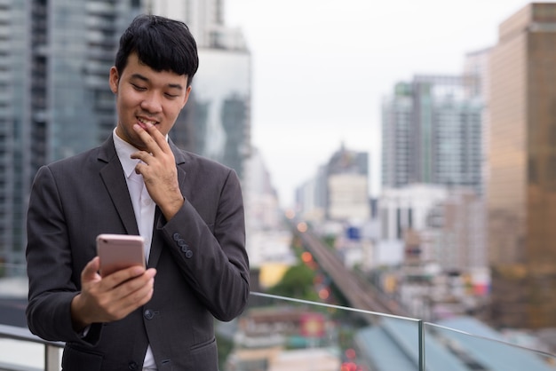 Retrato de joven empresario asiático con teléfono contra la vista de la ciudad