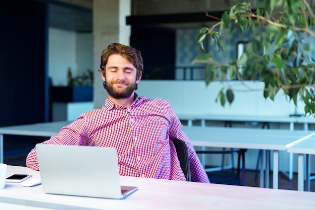 Retrato de joven empresario caucásico con ordenador portátil en su lugar de trabajo en la oficina moderna