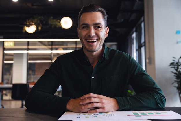 Retrato de un joven empresario caucásico sonriente discutiendo en una videollamada en una oficina creativa. Negocios inalterados, creativos, en línea, internet, comunicación.