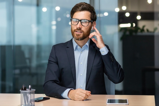 Retrato de un joven empresario consultor sentado en la oficina en la mesa hablando con la cámara