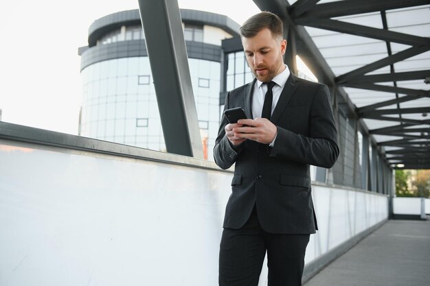 Retrato de un joven empresario emocionado vestido con traje sosteniendo un teléfono móvil celebrando