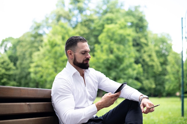 Retrato de un joven empresario físicamente apto fuma cigarro cubano en el parque y habla por teléfono móvil