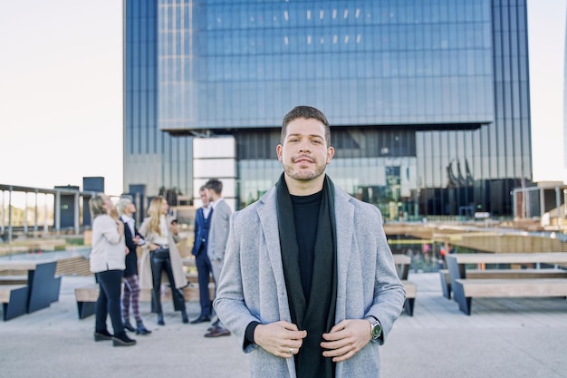 retrato de un joven empresario latino mirando la cámara con su equipo de trabajo en el fondo hablando fuera de foco