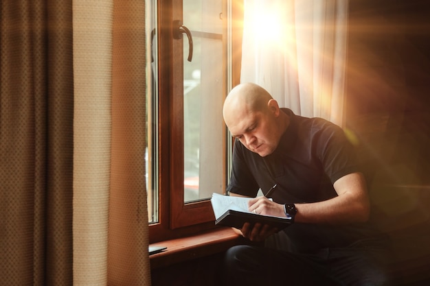 Retrato de joven empresario con portátil y teléfono en la ventana del salón en casa de campo. Hombre adicto al trabajo en ropa casual de casa trabajando en vacaciones. Inspiración creativa y puesta en marcha de empresas.