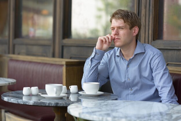 Retrato de joven empresario rubio guapo relajándose en la cafetería al aire libre