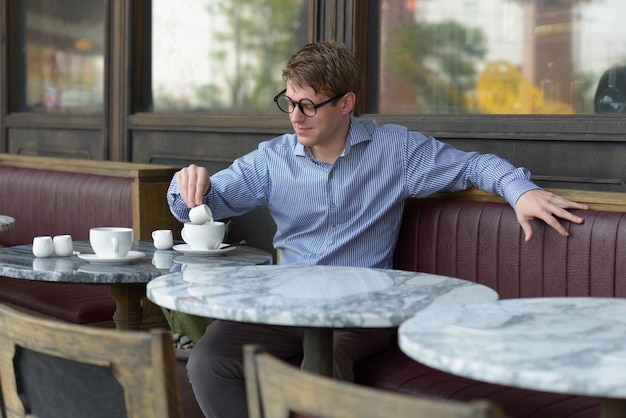 Retrato de joven empresario rubio guapo relajándose en la cafetería al aire libre