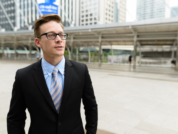 Retrato de joven empresario rubio guapo en traje en el puente Skywalk en la ciudad al aire libre