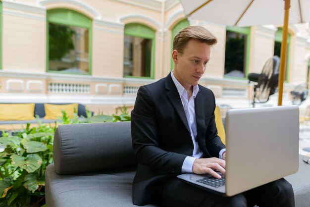 Retrato de joven empresario rubio guapo en traje de relax en la cafetería al aire libre