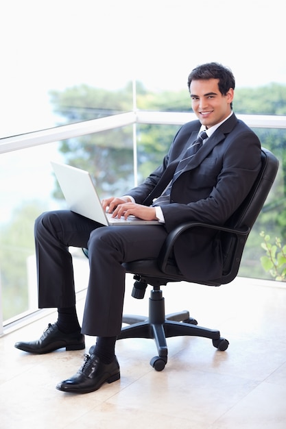 Retrato de un joven empresario sentado en un sillón trabajando con una computadora portátil