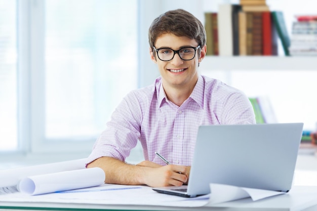 Retrato de un joven empresario sonriente trabajando en planos en la oficina