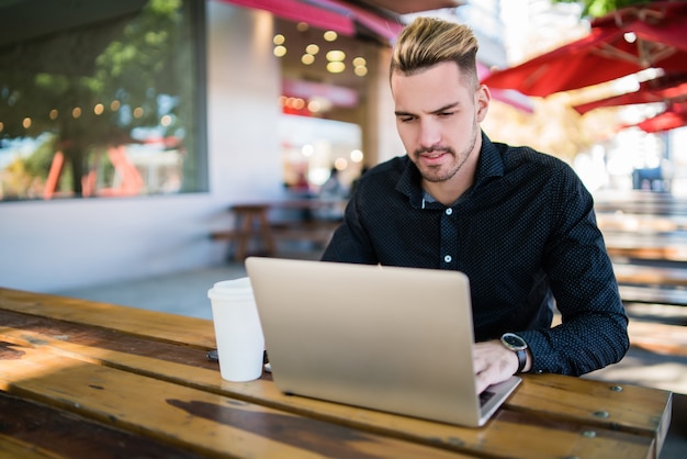 Retrato de joven empresario trabajando en su computadora portátil mientras está sentado en una cafetería. Concepto de tecnología y negocios.