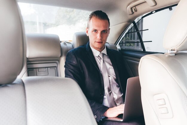 Foto retrato de un joven empresario usando una computadora portátil mientras está sentado en un coche