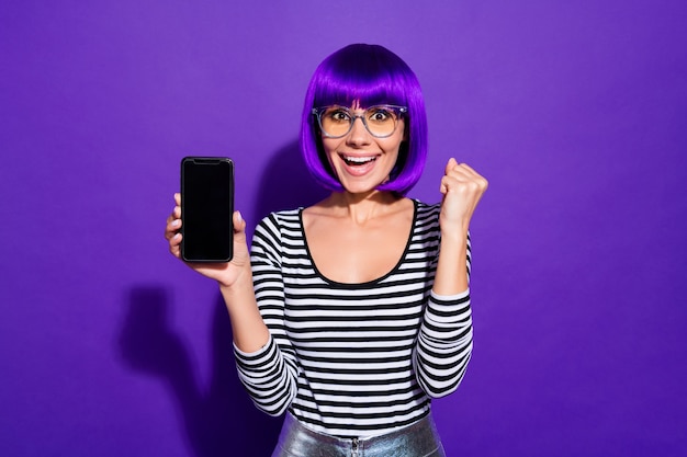 Retrato de joven encantadora impresionada sosteniendo gadget levantando puños gritando wow omg aislado sobre fondo violeta púrpura