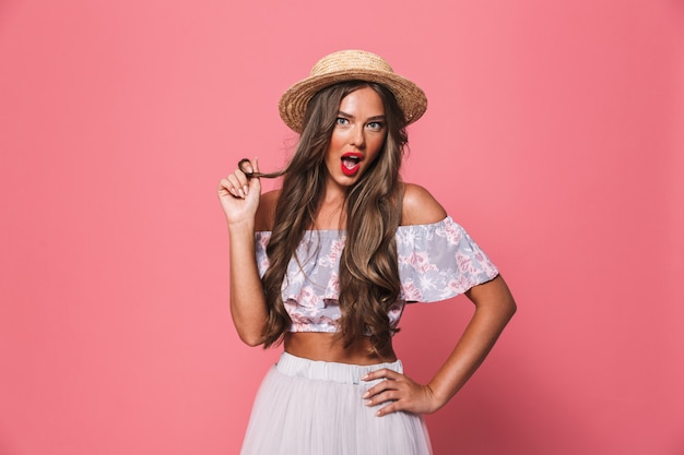 Retrato de joven encantadora con sombrero de paja sonriendo y tocando su hermoso cabello castaño