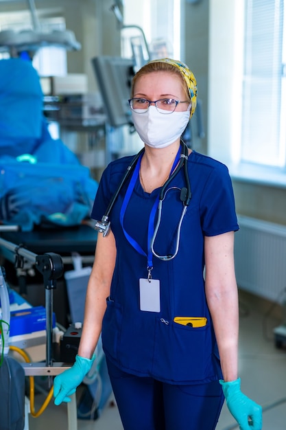 Retrato de joven enfermera quirúrgica en matorrales de pie en quirófano. Retrato de doctora en sala médica moderna.