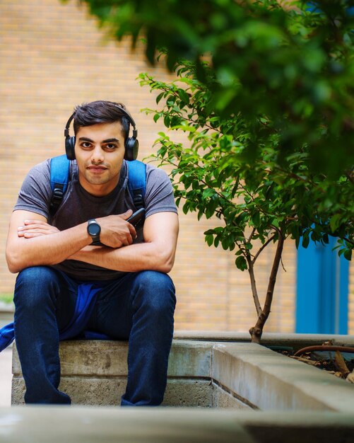 Retrato de un joven escuchando música mientras está sentado contra las plantas