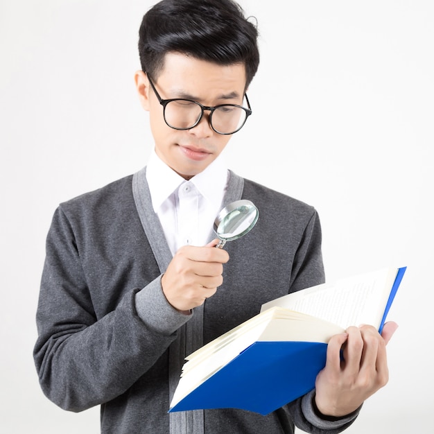 Retrato de un joven estudiante de asia con lupa para leer el libro. foto de estudio con fondo blanco. concepto para la educación