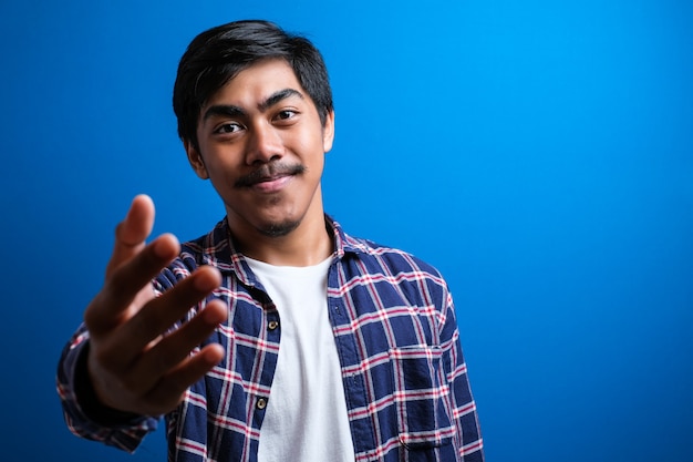 Retrato de joven estudiante asiático guapo vistiendo camisa de franela que ofrece apretón de manos contra el fondo azul aislado. concepto de acuerdo