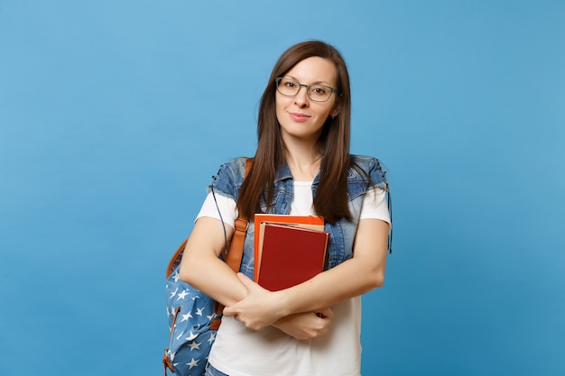 Retrato de joven estudiante atractiva mujer agradable con gafas con mochila mantenga libros escolares, listo para aprender aislado sobre fondo azul. Educación en el concepto de colegio universitario de secundaria.