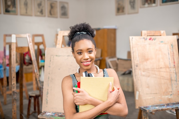 Retrato de un joven estudiante de etnia africana sosteniendo libros en el estudio para pintar