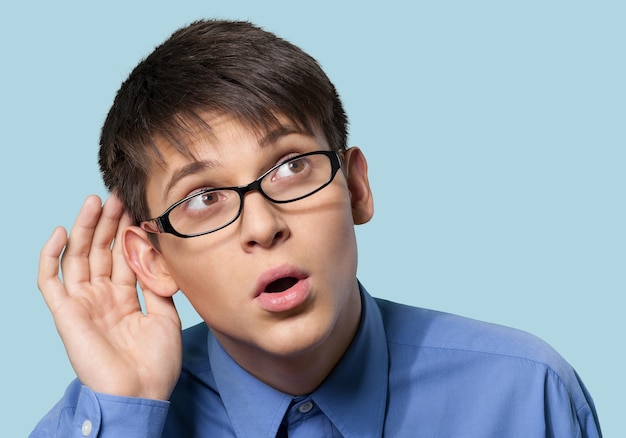 Retrato de joven estudiante guapo con gafas escuchando con gesto de mano