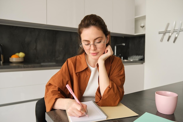 Foto retrato de una joven estudiante haciendo su tarea estudiando en casa sentada en la cocina tomando notas