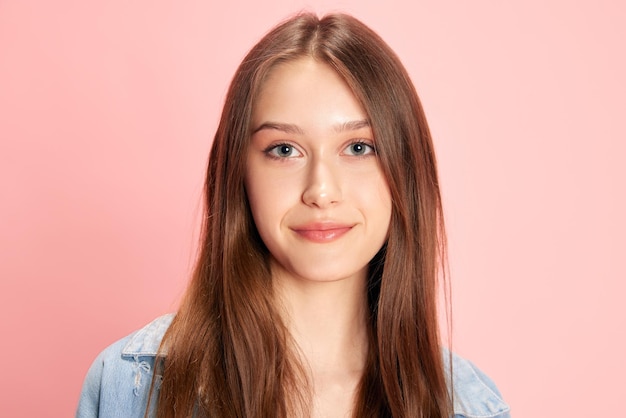 Retrato de una joven estudiante hermosa mirando a la cámara y sonriendo contra el estudio rosa