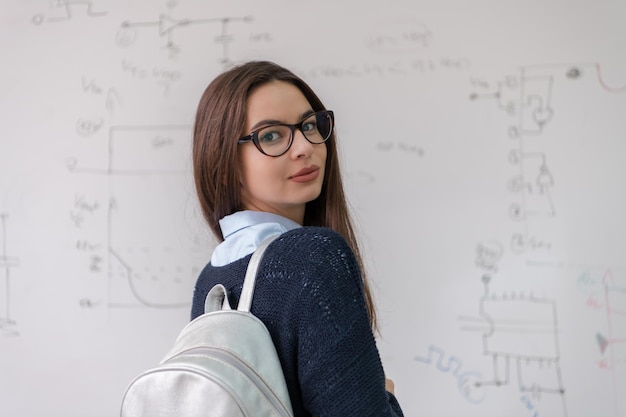 retrato de una joven estudiante hermosa parada frente a una pizarra blanca y mirando la cámara