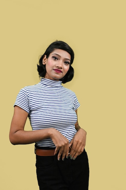 Foto retrato de una joven estudiante india mirando a la cámara de pie sobre un fondo de estudio amarillo