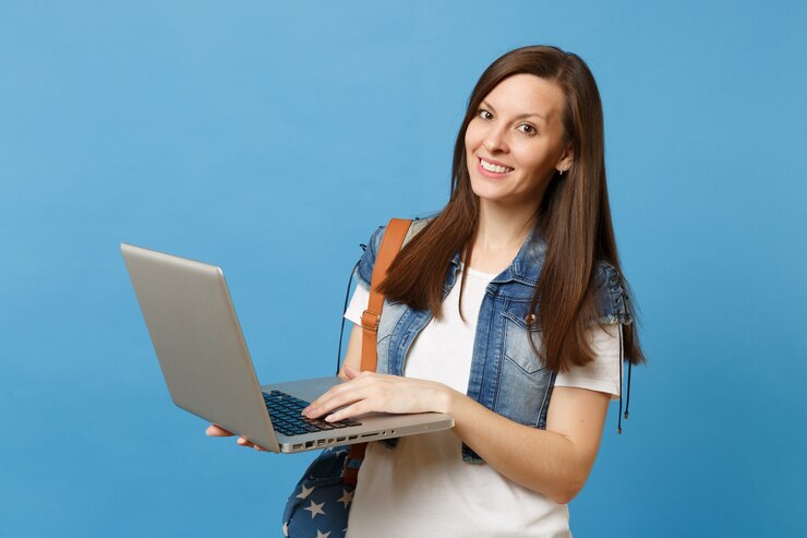Foto retrato de joven estudiante mujer bonita en ropa de mezclilla con mochila sosteniendo y usando trabajando en equipo portátil aislado sobre fondo azul. educación en la universidad. copie el espacio para publicidad.
